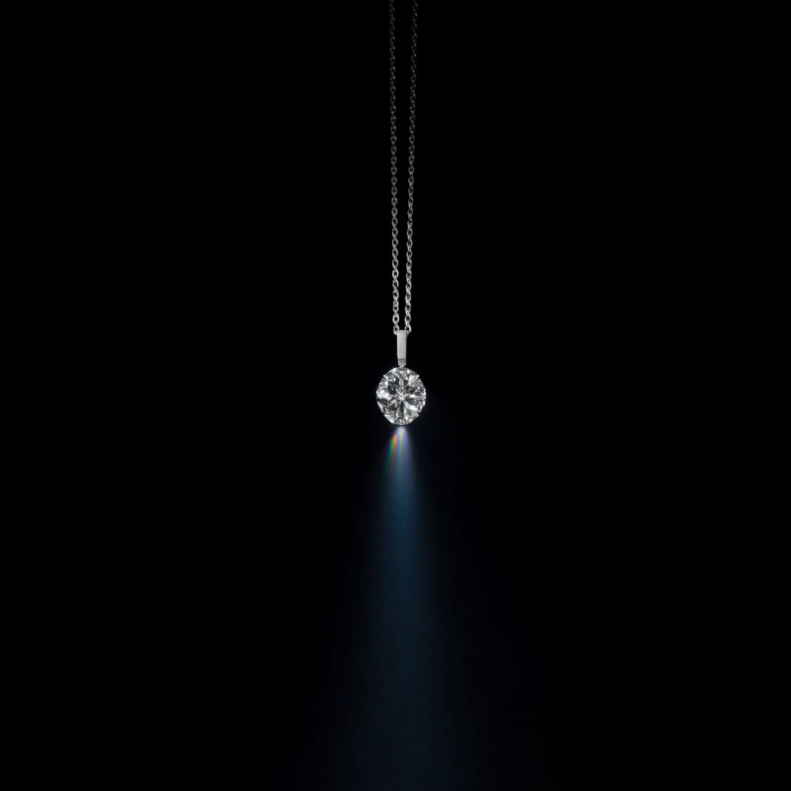 Diamond solitaire pendant on a fine chain against black, a narrow prism flare crossing the frame.