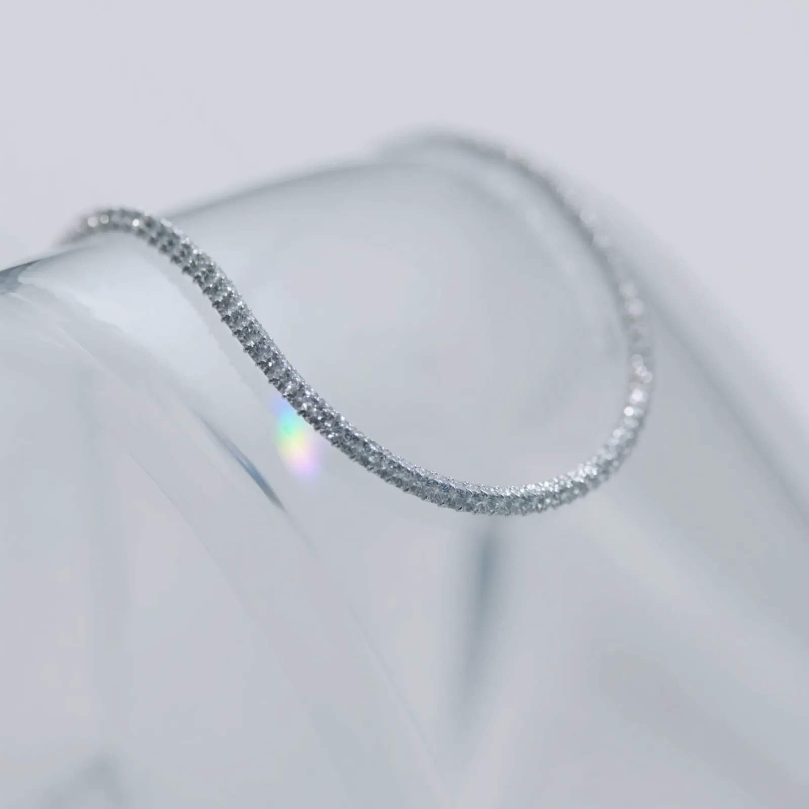 Slim pavé diamond bangle resting on the curved edge of a clear glass form.