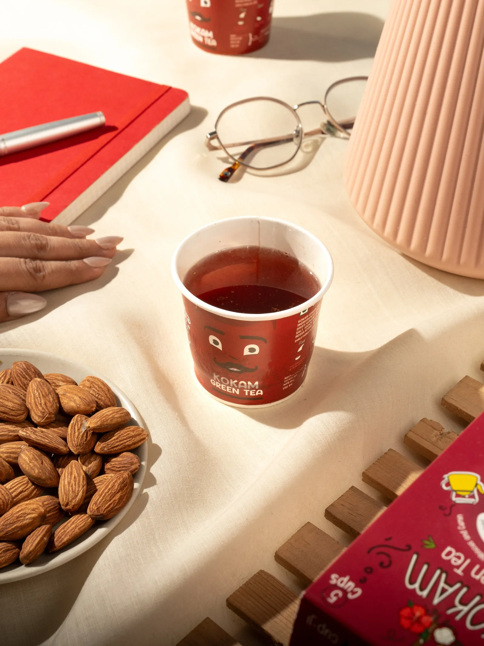 Kokam cup on a cream desk with almonds, reading glasses, a notebook and stacked Jenga blocks.