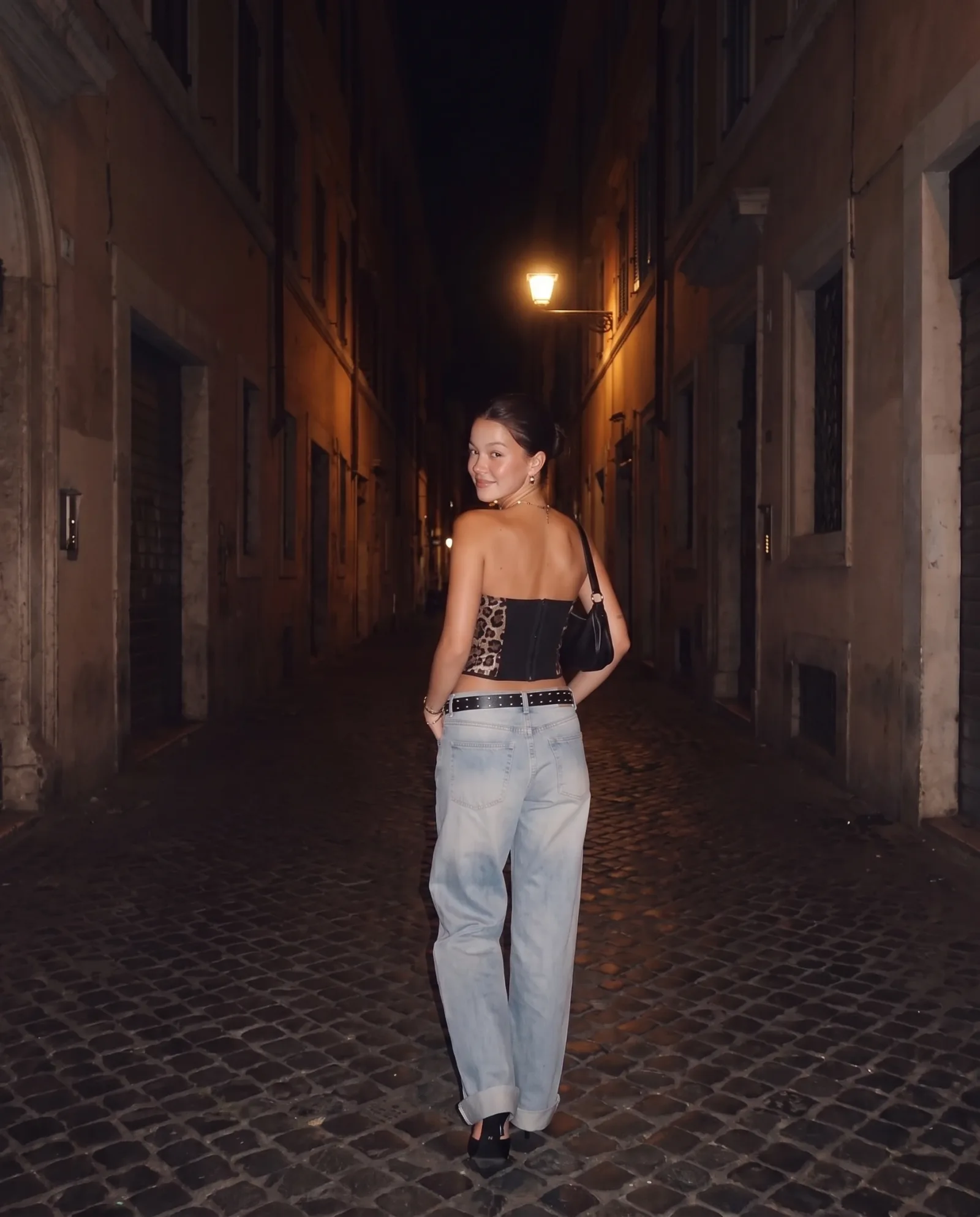Back view of the leopard corset and jeans in a narrow alley, looking back over the shoulder.