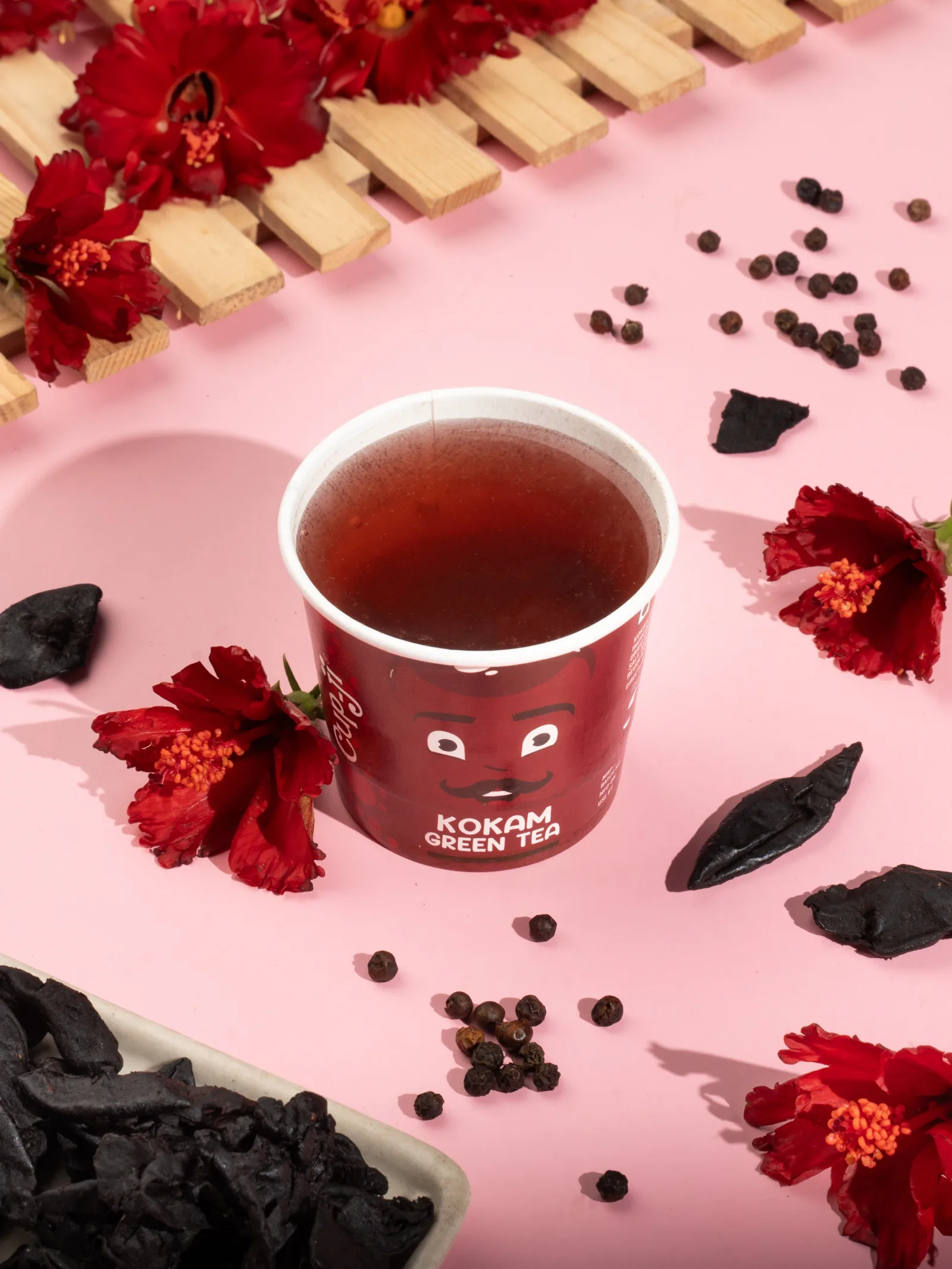 Kokam cup with hibiscus flowers and dried kokam rind on a pink surface.