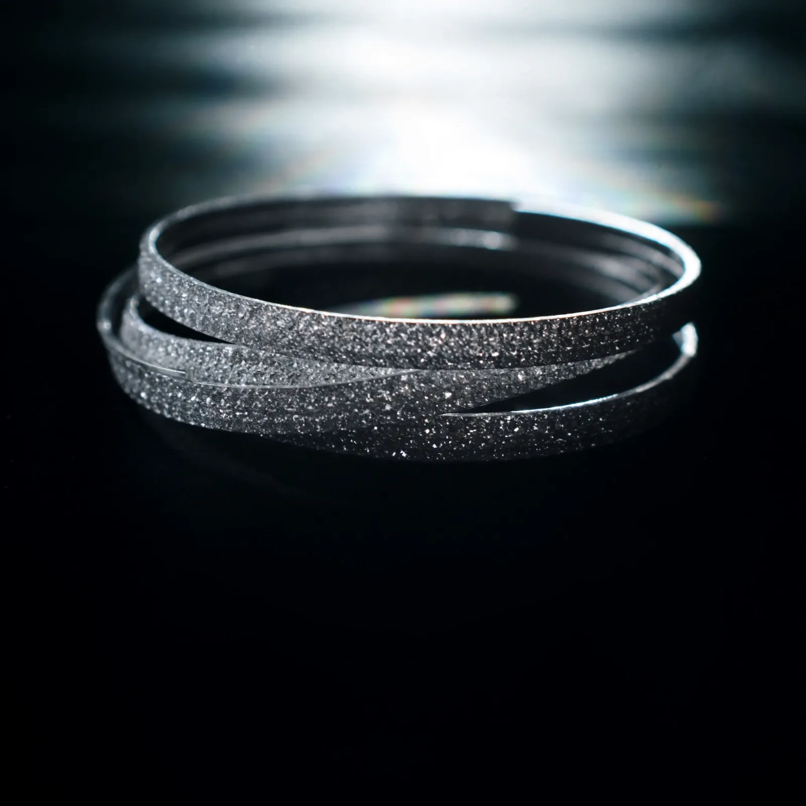 Set of slim diamond-set bangles stacked and overlapping on a dark reflective surface.