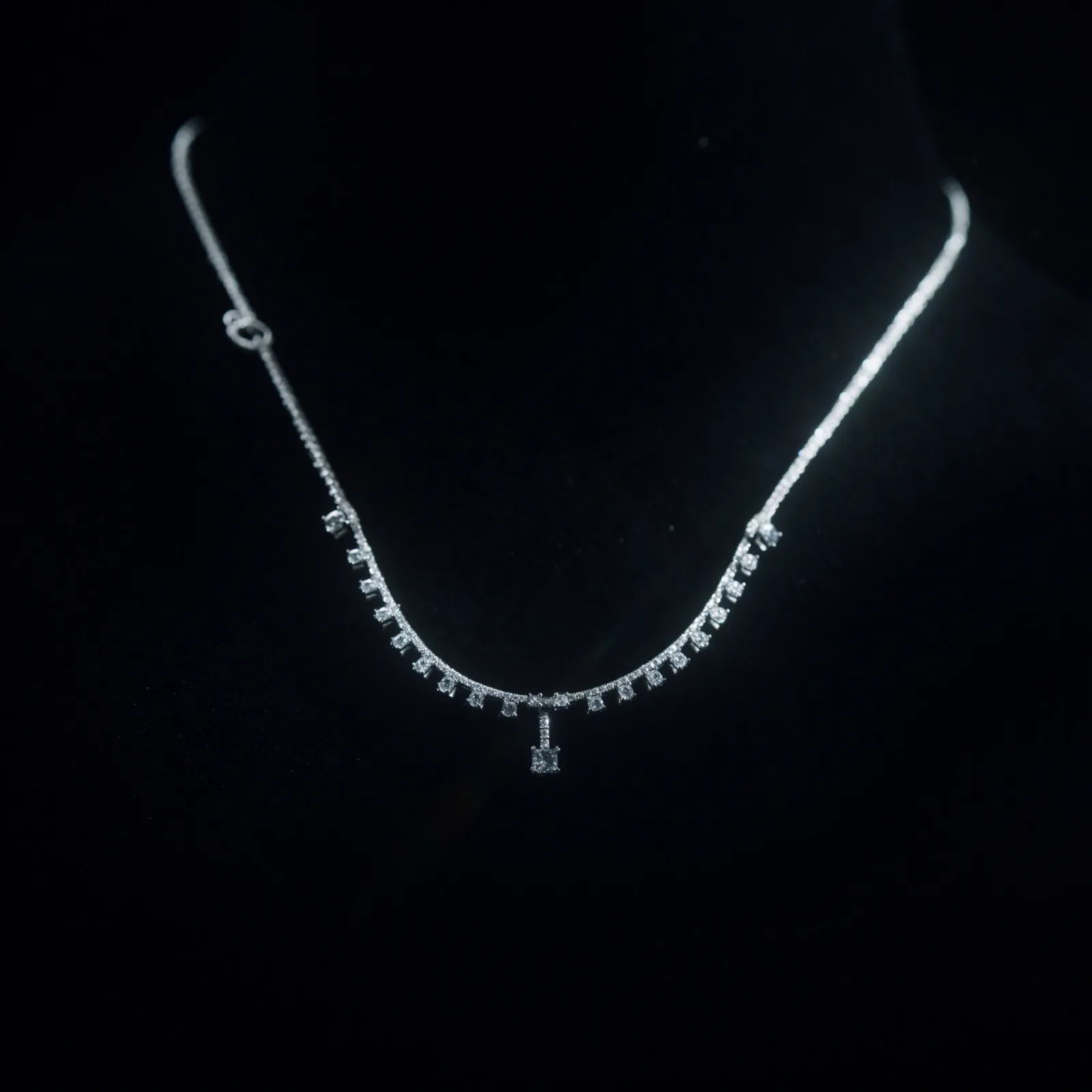 Diamond necklace with graduated drops along the front and a single solitaire at the centre, on a dark bust.