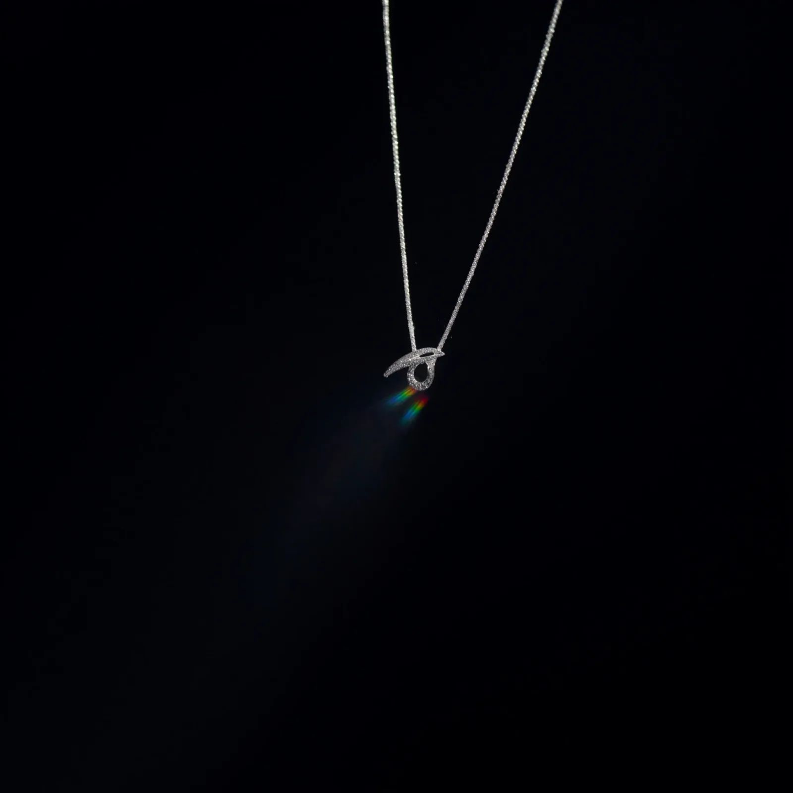 Fine chain necklace with a small pavé diamond motif pendant against a dark background.