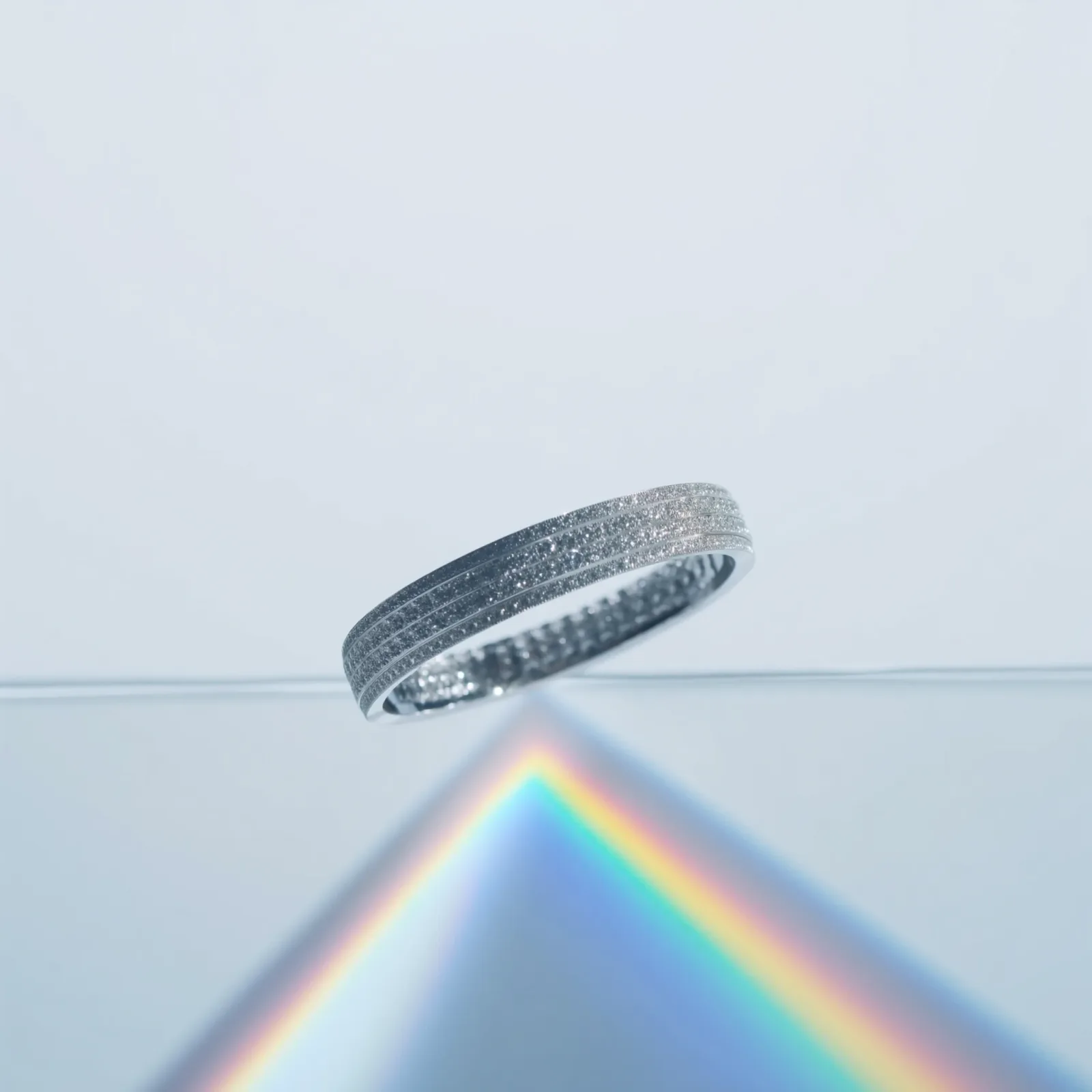 Multi-row pavé diamond bangle photographed above a pale surface with a spectrum fanning out beneath it.