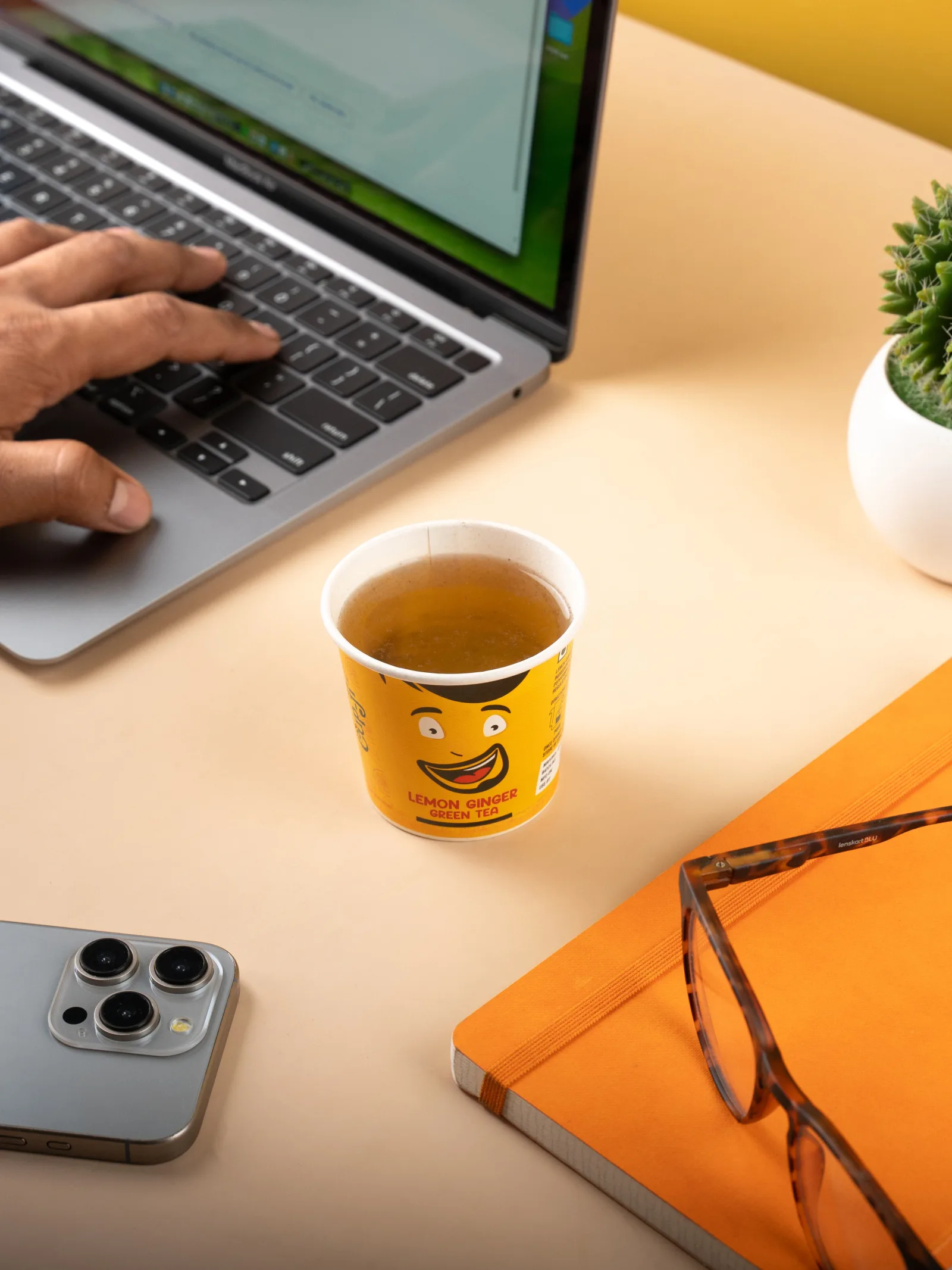 Lemon Ginger cup beside a laptop on a desk in natural window light.