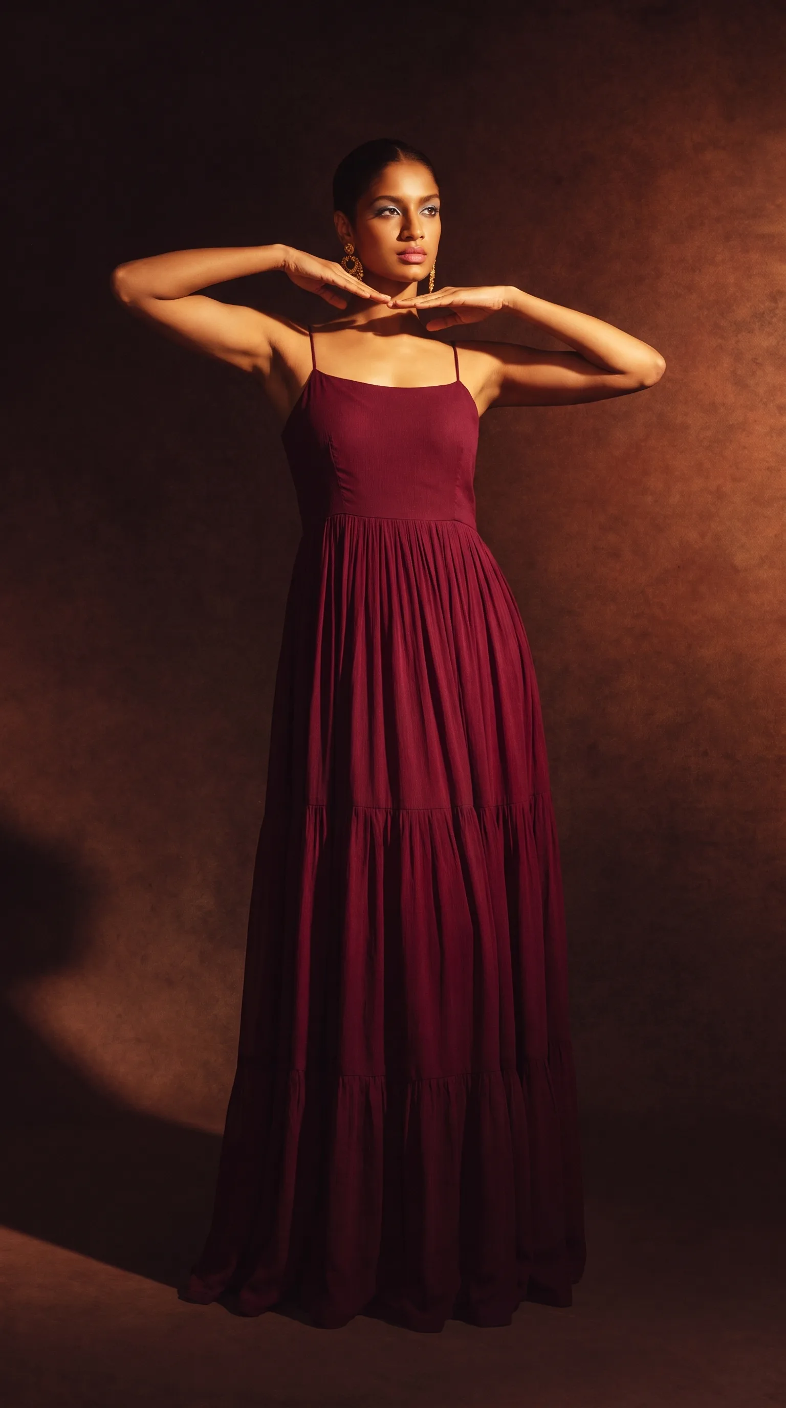 The patchwork shrug gown with belt, woman standing with both arms raised, photographed against a flat teal panelled wall.