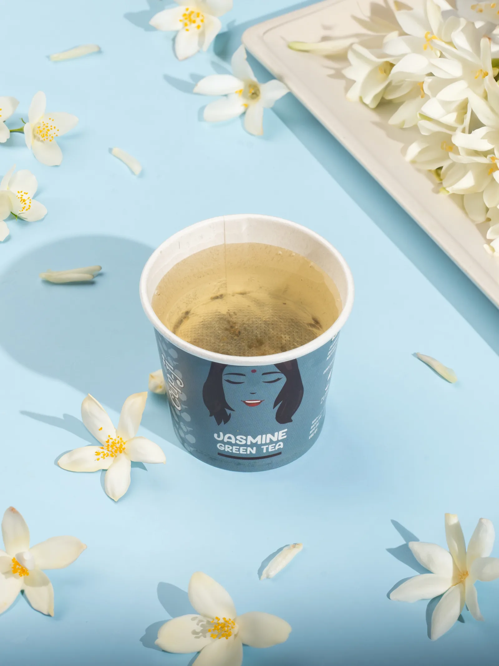 Jasmine cup surrounded by fresh white jasmine flowers on a pale blue surface.