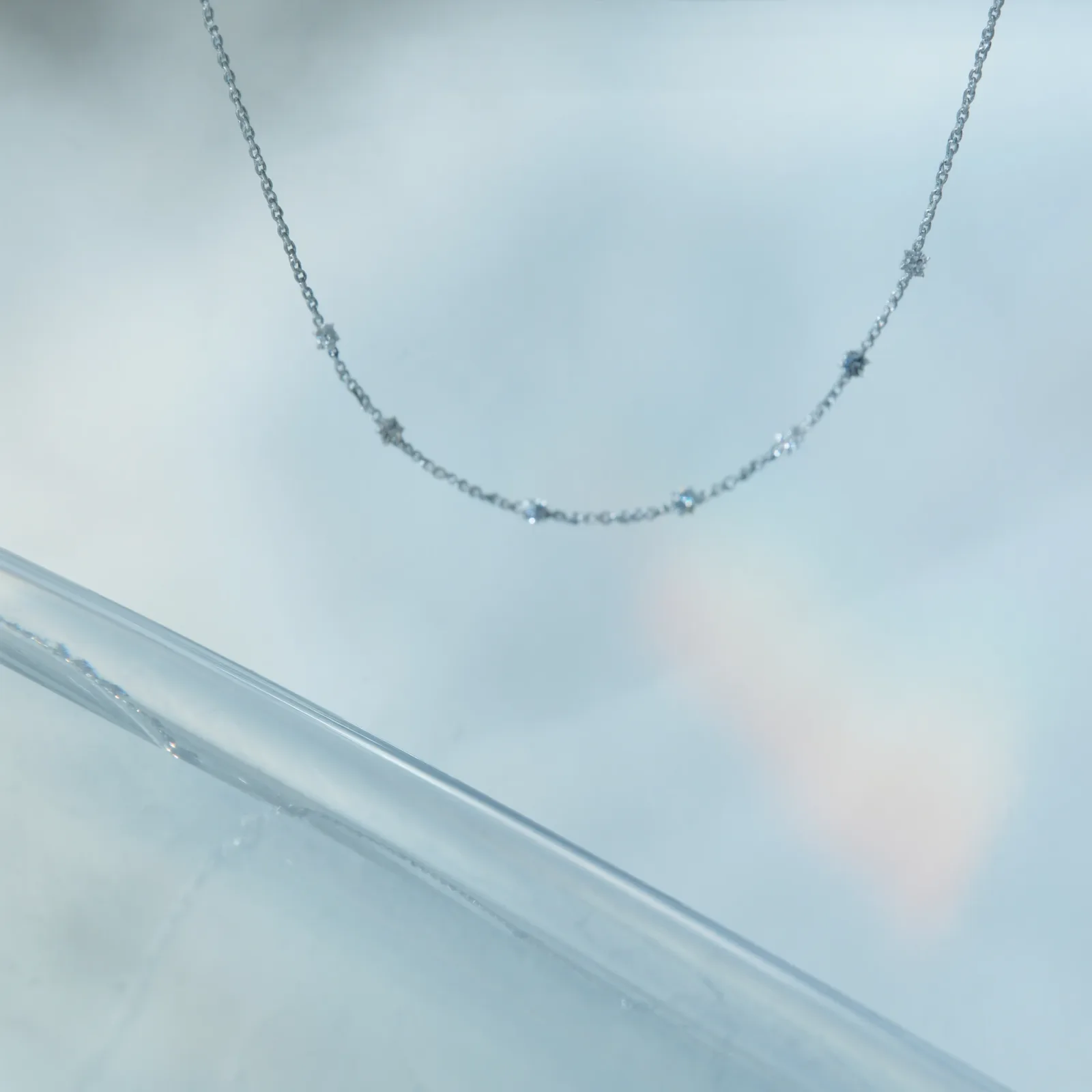 Diamonds-by-the-yard station necklace on a pale blue background, bezel-set stones spaced along a fine chain.