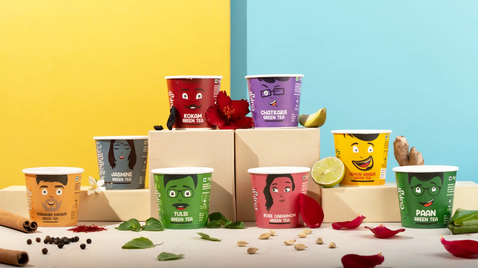 Eight Cupji flavour cups staged at different heights on blocks, surrounded by their spices and flowers, against a split yellow and blue background.
