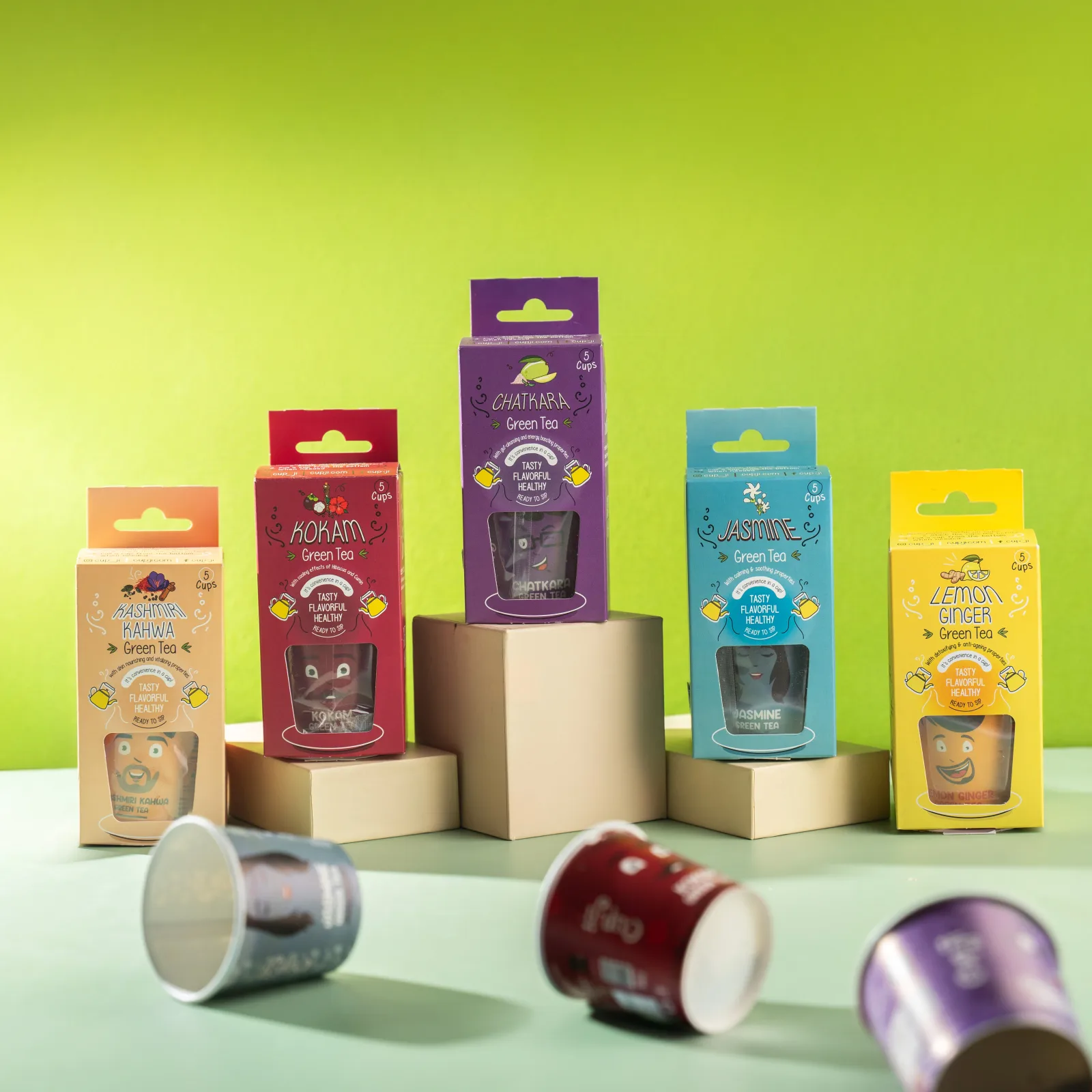 Five Cupji five-cup boxes arranged on graduated cream risers against a green background, loose cups in the foreground.