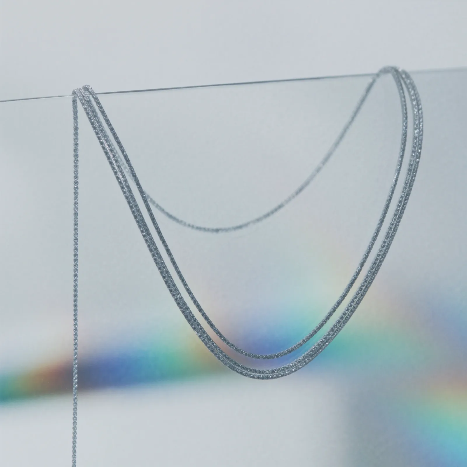 Diamond-set chain hanging in a long curve against black, the links catching light down its length.