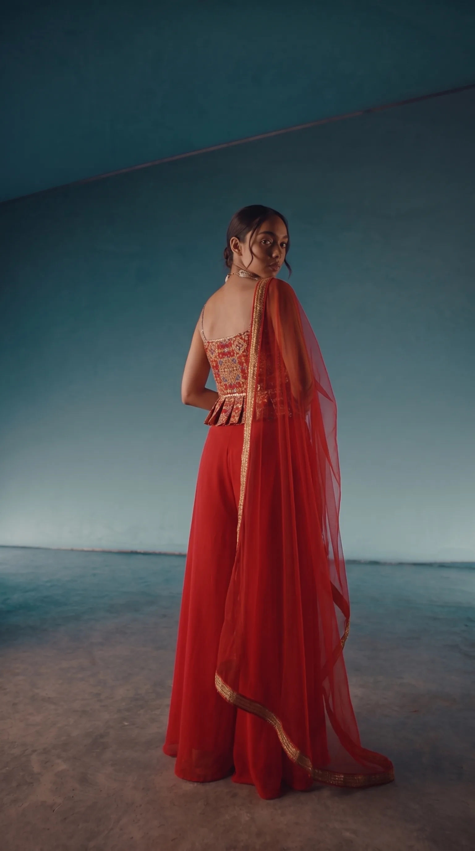 Back view of the peplum top and red palazzo, woman with a hand on her hip glancing back, the peplum back pleat and dupatta drape visible.