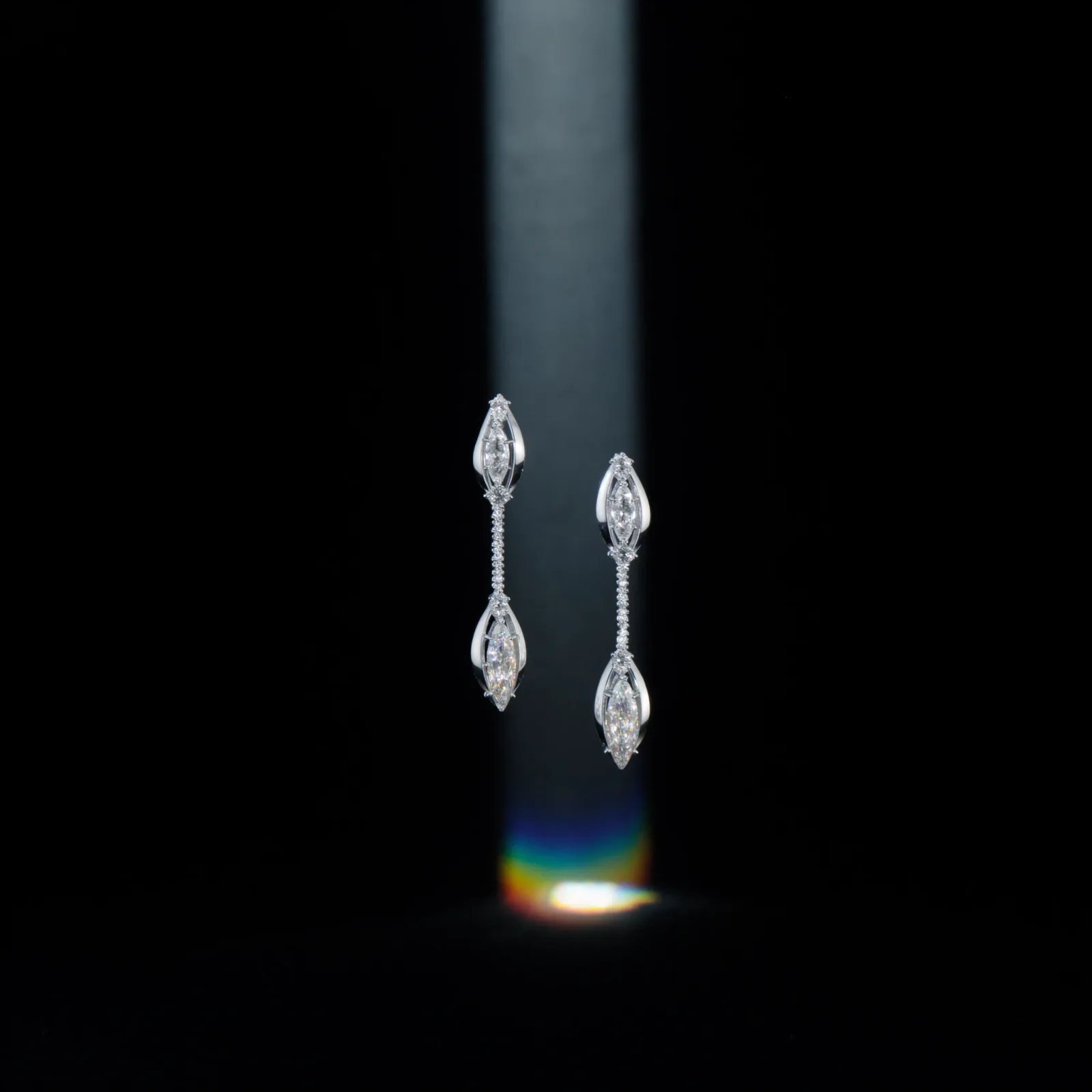Pair of marquise diamond drop earrings lit by a narrow shaft of light against a dark background.