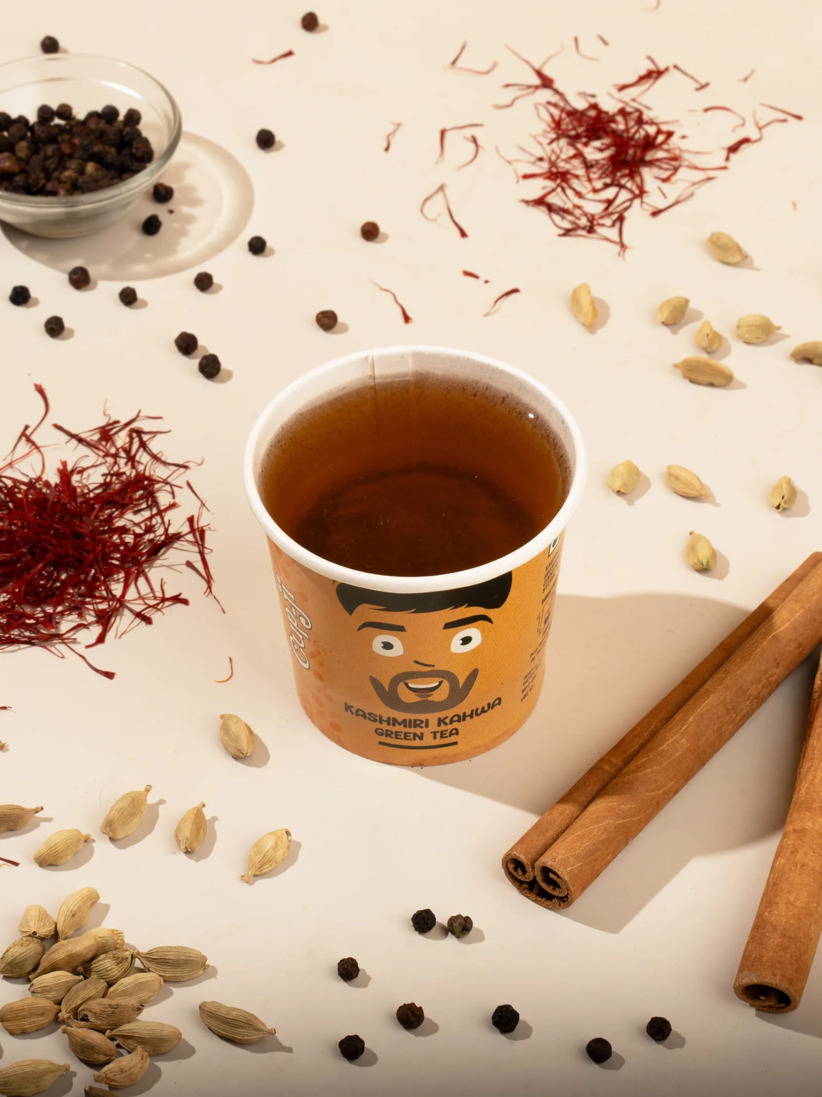 Kashmiri Kahwa cup styled with saffron threads, cinnamon bark, green cardamom and black peppercorns on a warm ground.