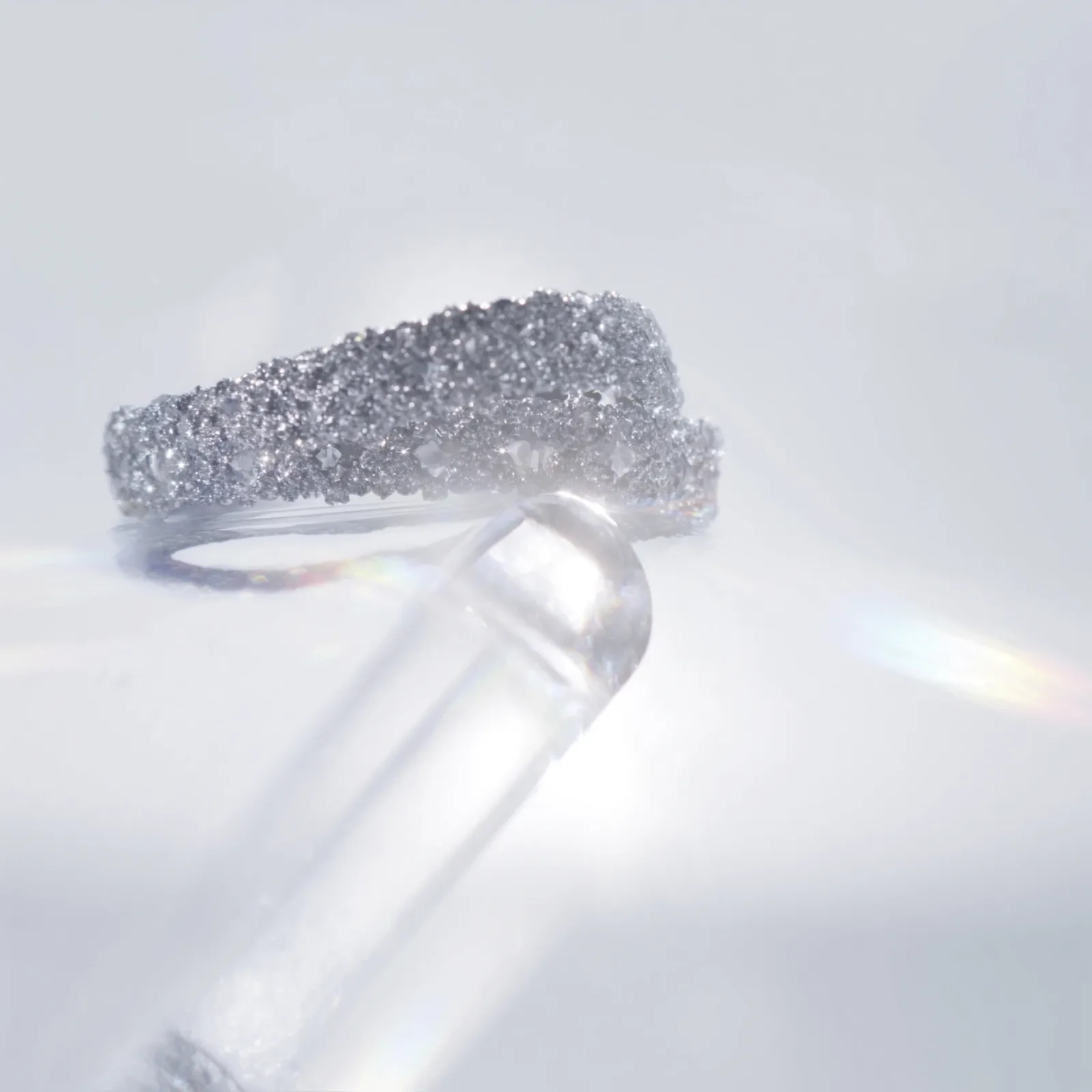 Wide pavé diamond bangle resting on a clear glass rod against a dark background.