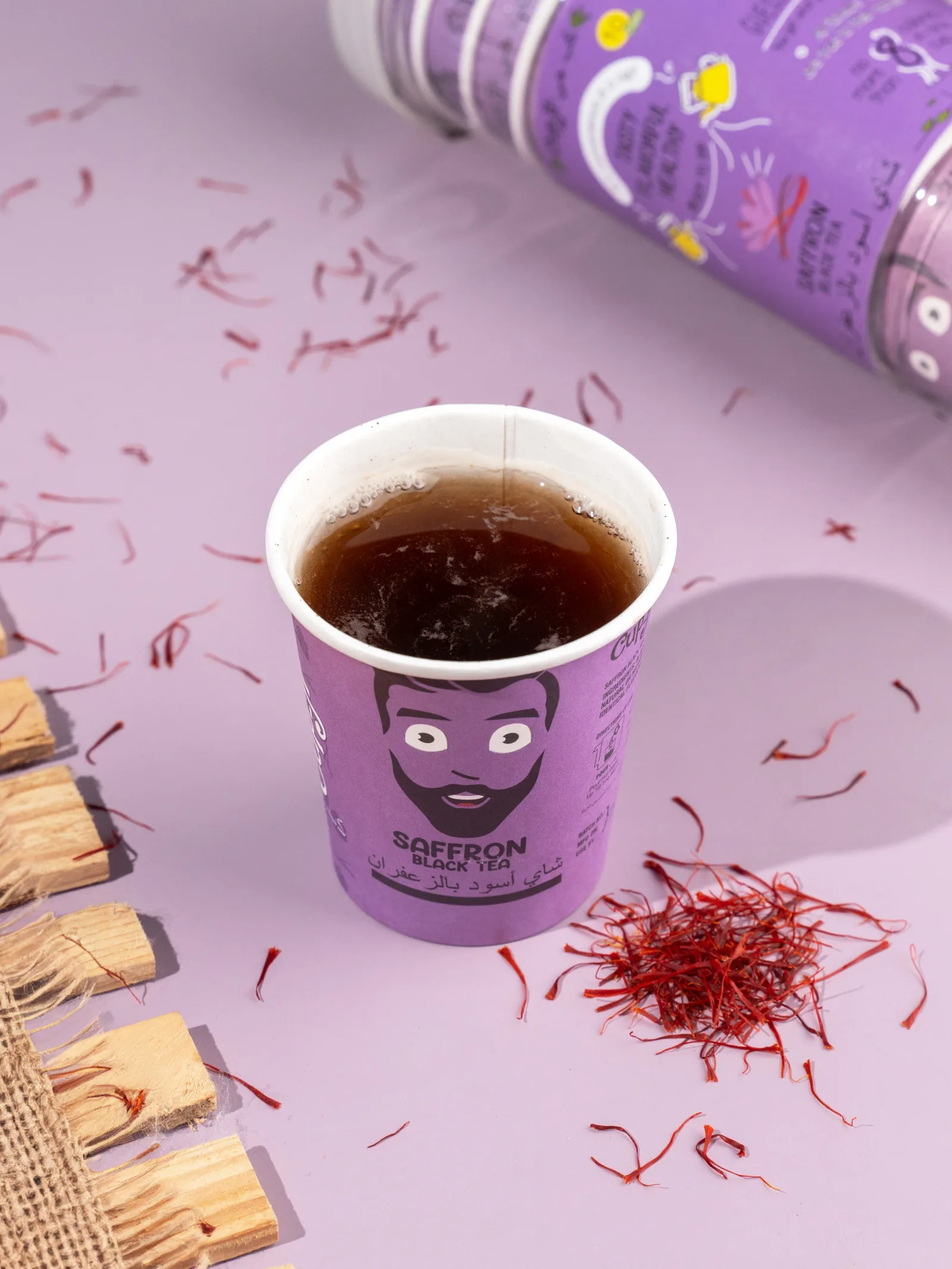 Brewed Saffron Black Tea cup on a lavender surface with loose saffron threads and wood chips.