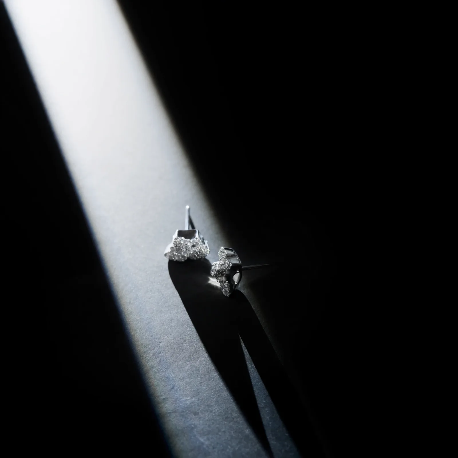 Pair of diamond stud earrings lit by a narrow shaft of light against a dark background.