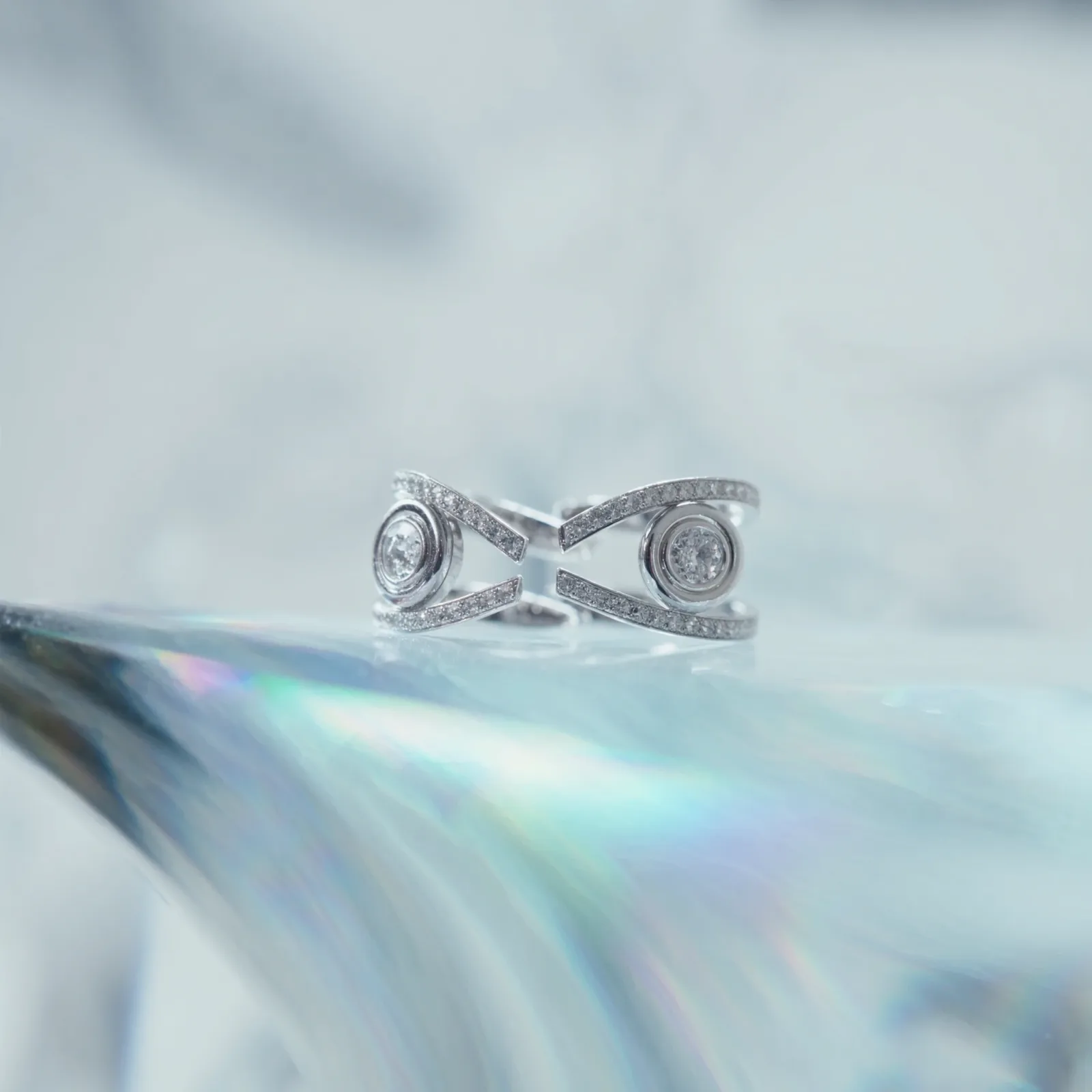 Pair of open cuff earrings with bezel-set round diamonds and pavé edges, on an iridescent surface.