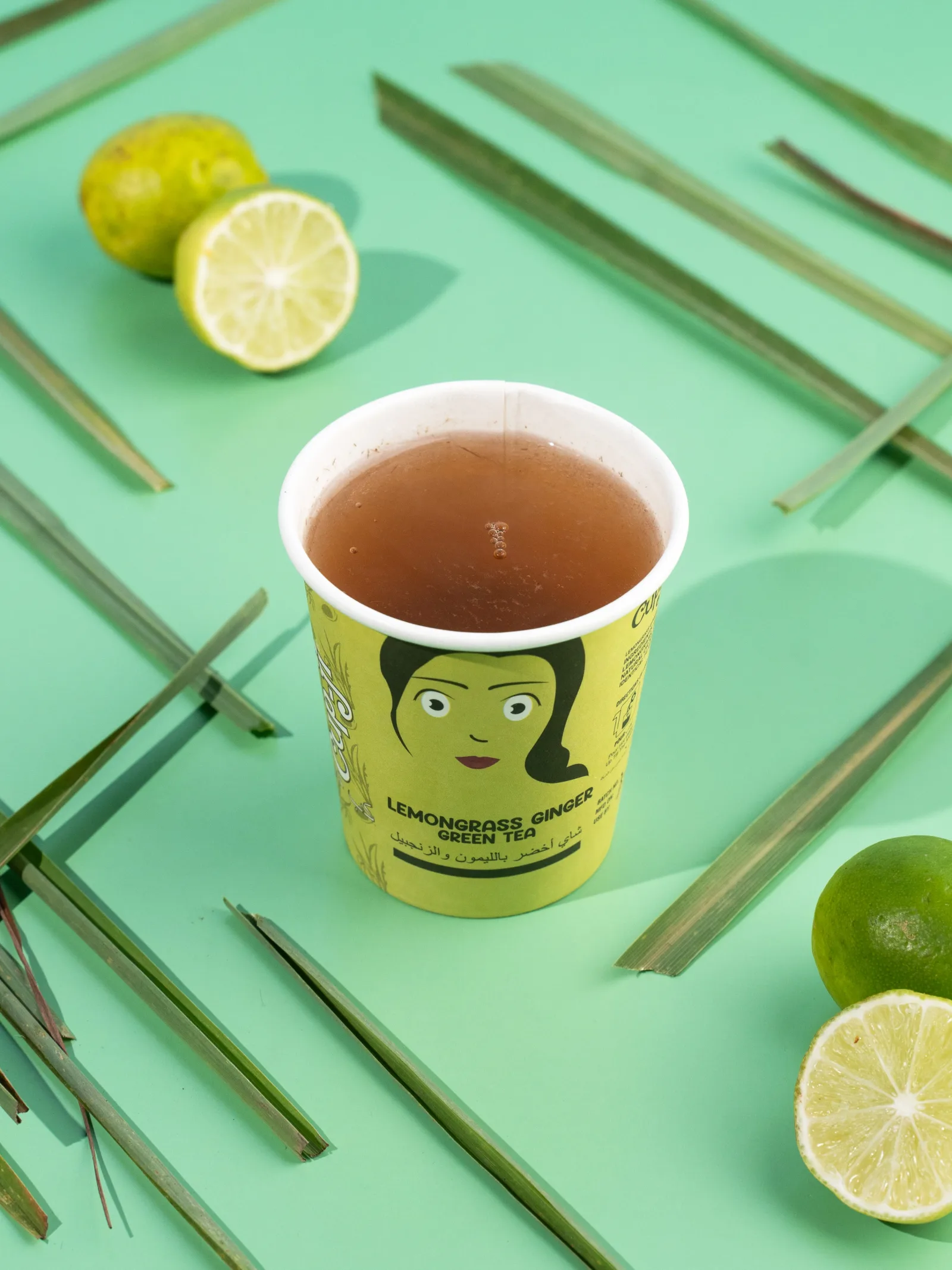 Brewed Lemongrass Ginger cup with lemongrass blades and halved limes.