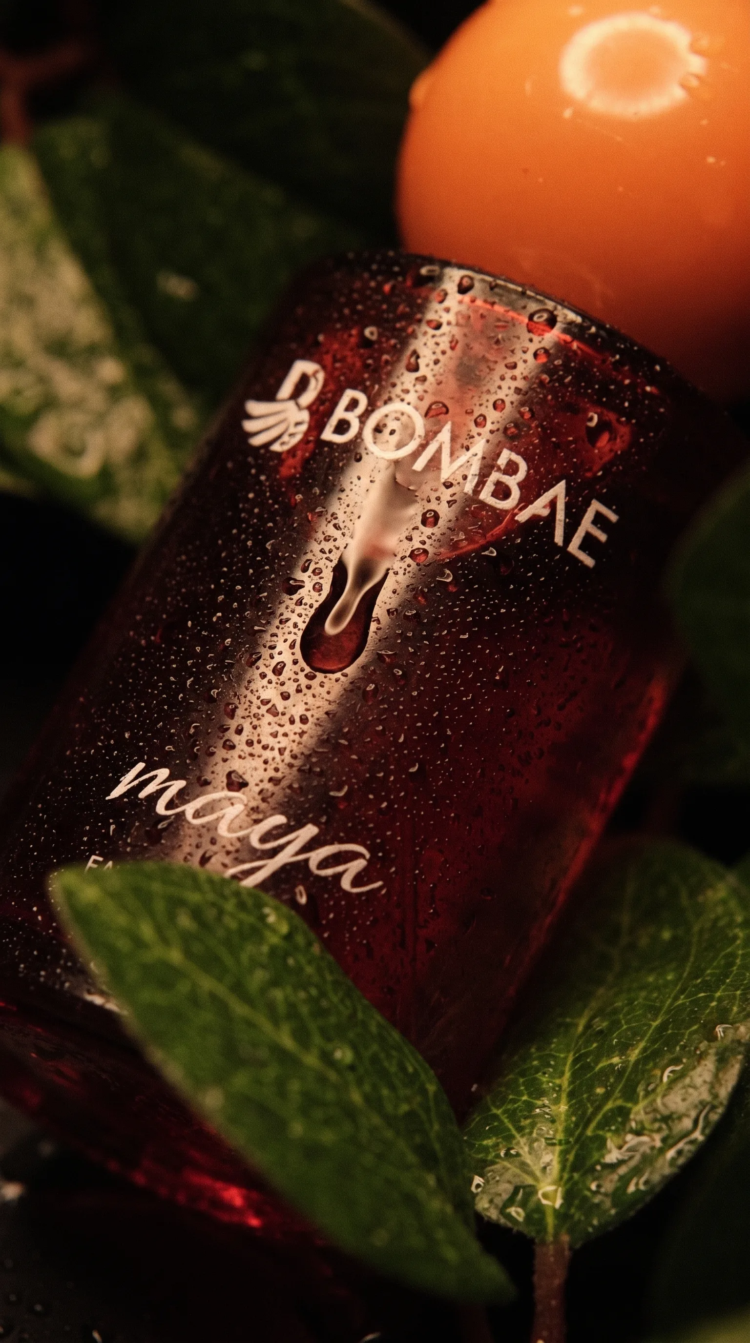 Extreme close-up of the wet Bombae Maya glass label, water droplets running down over the engraved logo and name.