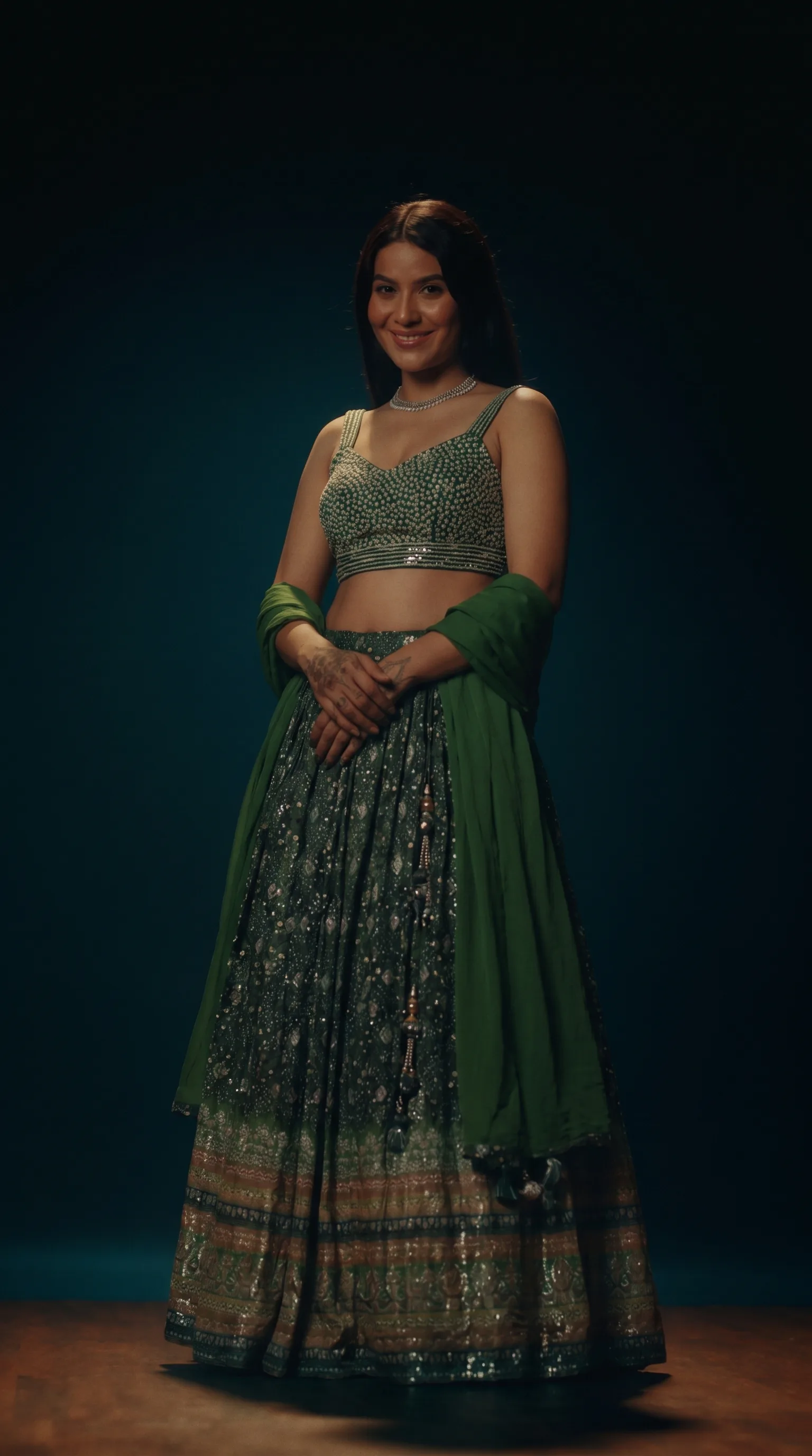 The green ghaghara choli with the sequinned dupatta spread wide in both hands, photographed against a flat red background.