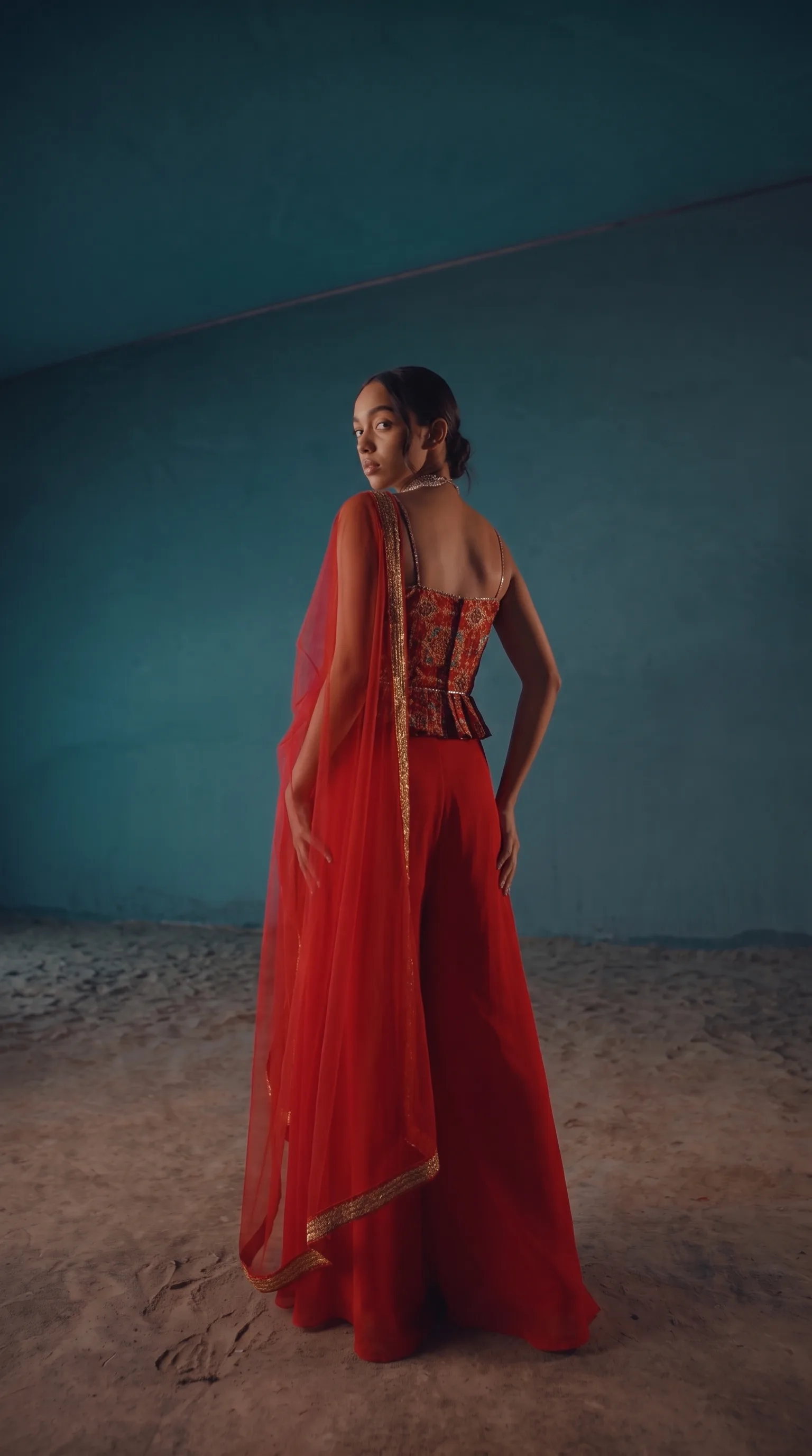 The same peplum top and red palazzo shot straight-on at full length, arms at the sides, same tunnel set and directional light.
