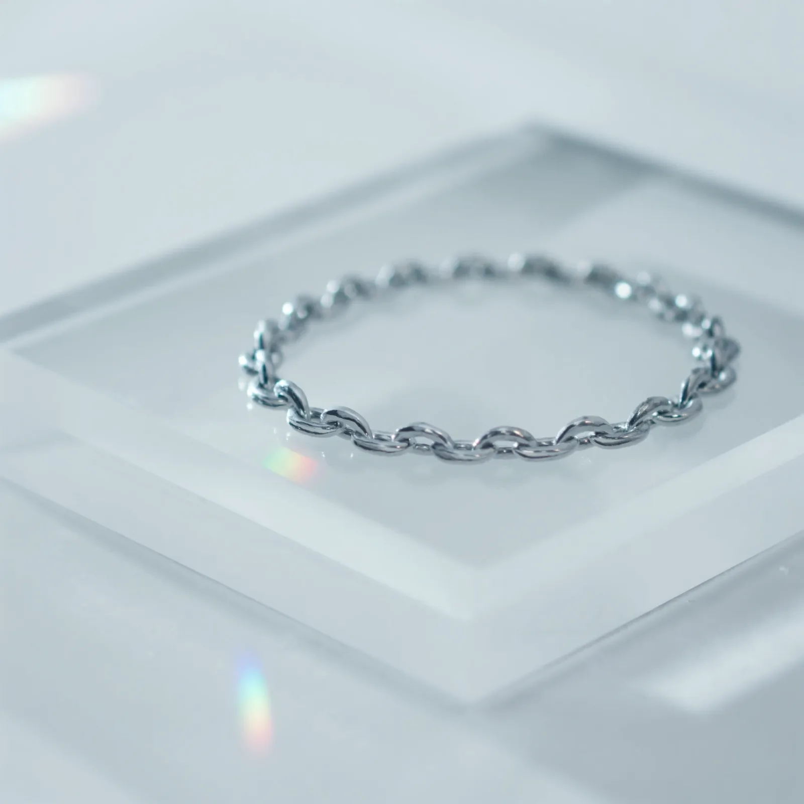 Polished cable-link chain bracelet laid in a circle on a frosted acrylic slab.