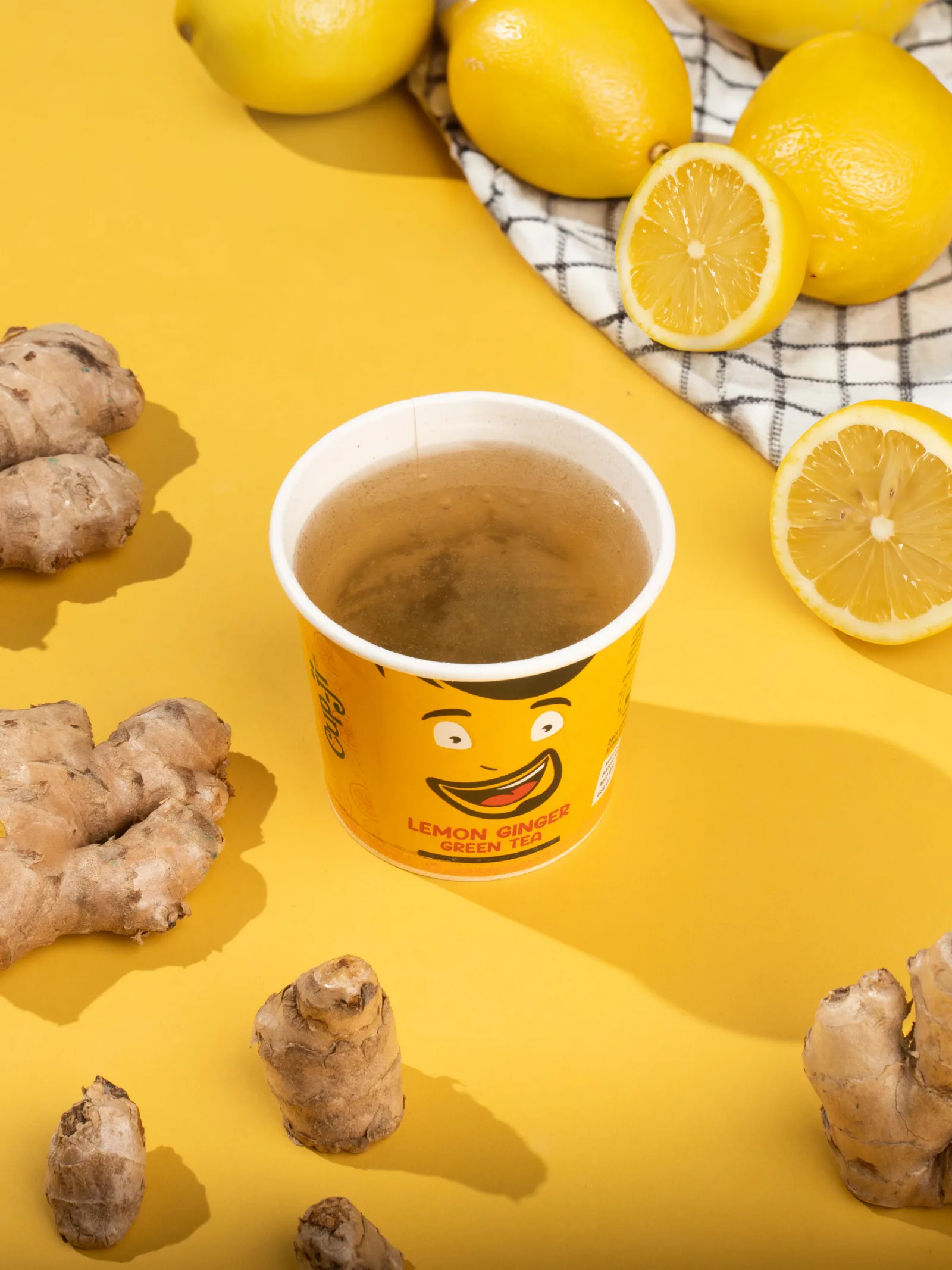 Lemon Ginger cup with halved lemons and fresh ginger root arranged on a yellow surface.