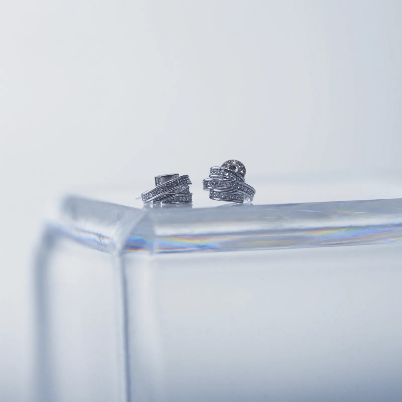 Pair of pavé diamond coil stud earrings on the edge of a clear acrylic block.