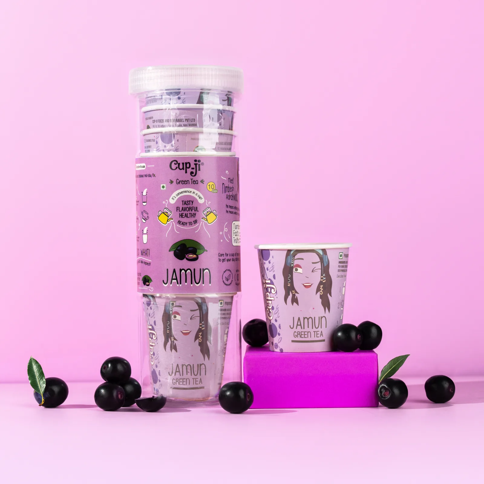 Jamun tube pack and a single cup on a pink ground with fresh jamun fruit and a purple block prop.