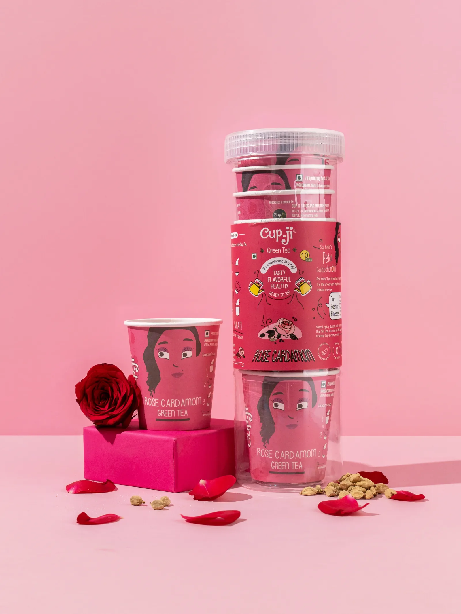 Rose Cardamom jar and cup on a pink ground with a red rose and scattered petals.