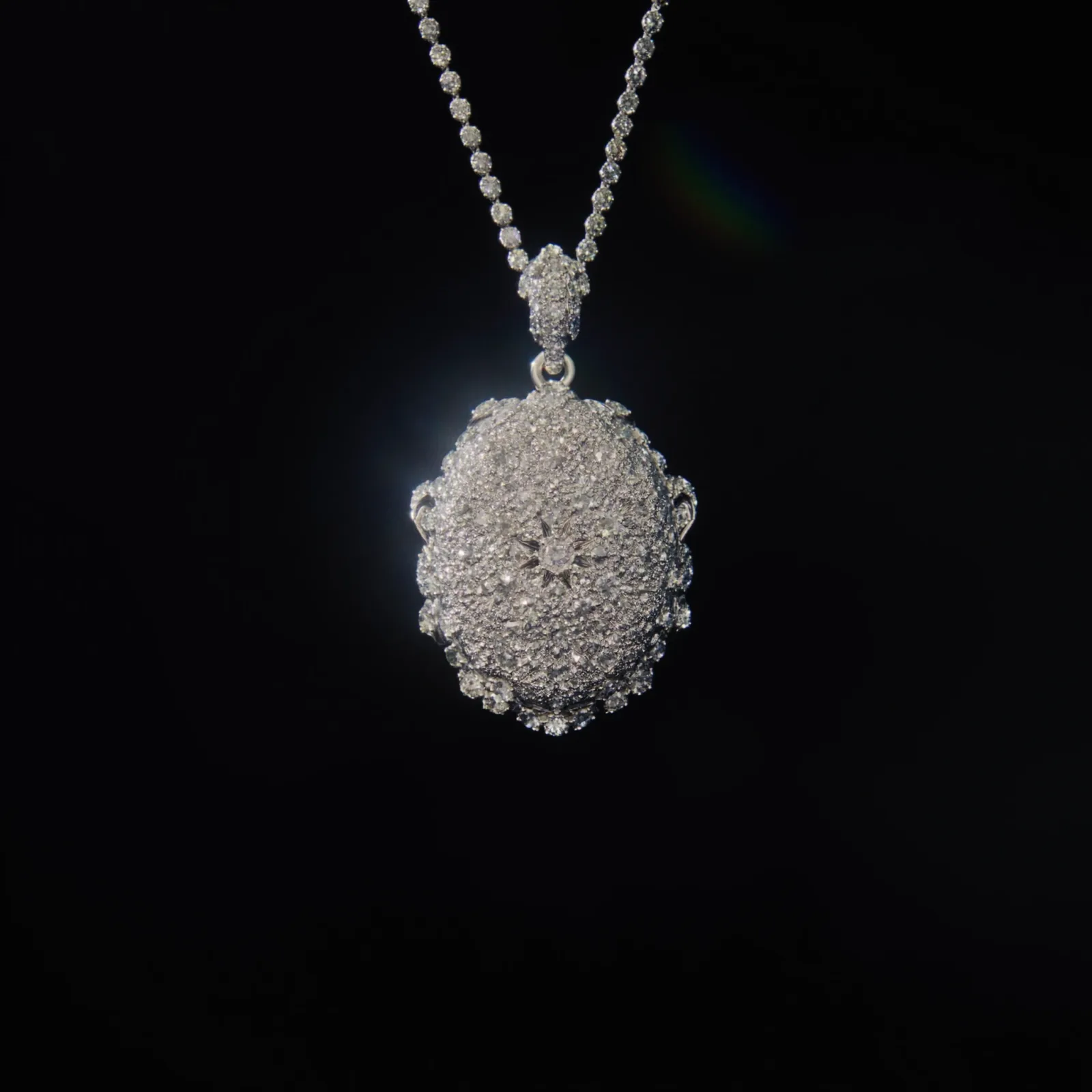 Pavé diamond oval pendant hanging from a diamond-set chain against a dark background.